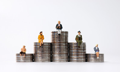 Miniature people sitting on piles of coins.