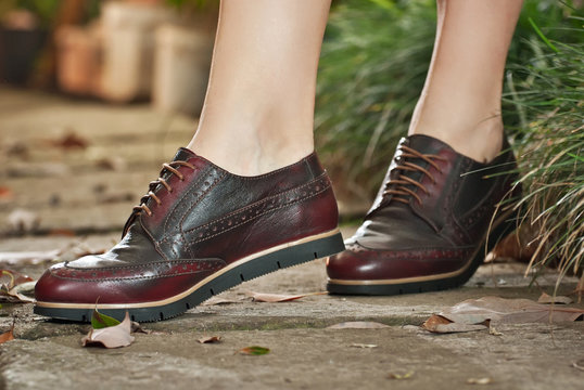 Women's leather boots close-up. The girl walks in shoes with a background of arrangeries with tropical plants. Oxford style shoes.