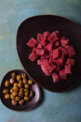 Raw beef pieces on a platter. Marinated olives on a saucer.