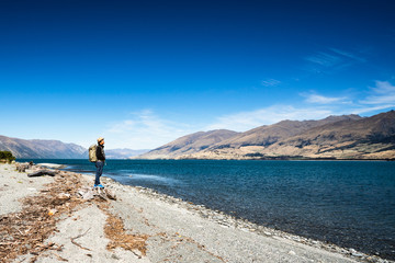 Fototapeta premium Tourist admires the view while stand next to Lake wanaka Boundary Creek with background of blue sky and rocky mountain with copy space.