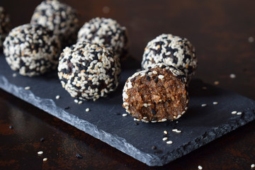 Healthy raw energy bites with flax seeds, almonds, banana and dates. Vegan truffles in sesame seeds on dark background. Homemade candy balls. Raw food. Gluten free. Dairy free.