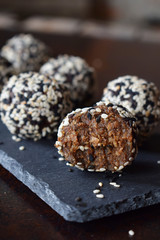 Healthy raw energy bites with flax seeds, almonds, banana and dates. Vegan truffles in sesame seeds on dark background. Homemade candy balls. Raw food. Gluten free. Dairy free.