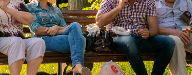 unidentified people sit on a wooden bench in the green park, chatting in a public places