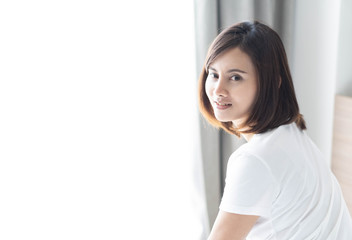 Woman sitting on bed in bedroom and looking from back with smile and happy feeling, selective focus