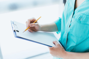 cropped shot of doctor in blue uniform writing on clipboard