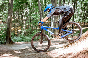 Fototapeta na wymiar Professional well equipped cyclist riding downhill on the off road in the forest. Concept of an extreme sport and enduro cycling