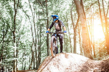 Professional well equipped cyclist standing on the hill while riding downhill in the forest. Concept of an extreme sport and enduro cycling