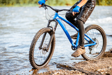 Fototapeta premium Professional well-equipped cyclist riding on the rocky riverside in the mountains. Close-up with no face