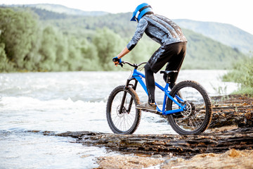 Professional well-equipped cyclist riding on the rocky riverside in the mountains. Concept of a freeride cycling and extreme sport