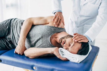 chiropractor massaging neck of man lying on Massage Table - obrazy, fototapety, plakaty