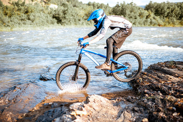 Professional well-equipped cyclist riding on the rocky riverside in the mountains. Concept of a freeride and off road cycling