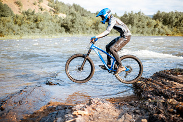 Fototapeta na wymiar Professional well-equipped cyclist riding on the rocky riverside in the mountains. Concept of a freeride and off road cycling