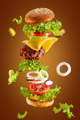 Big tasty home made burger with flying ingredients on white background.