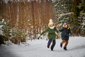 Fototapeta na wymiar Children boy and girl runing in snow forest in a winter day. Teenagers having trip and rest in weekend outdoor