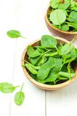 Fresh green spinach leaves on wooden bowl on white wooden rustic background top view copy space. Baby young spinach leaves, Ingredient for salad, healthy food, diet. Nutrition concept.