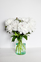 Bouquet of white peonies in a glass vase on white wall background