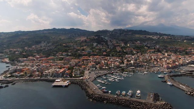 Aerial descending view of the fishing village of Aci Trezza in Sicily, with mount Etna in the background