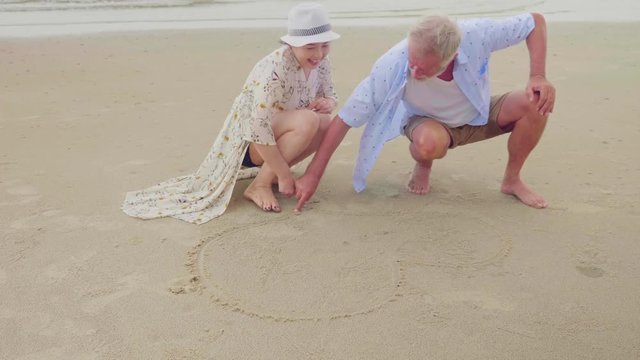 Happy senior couple drawing a heart shape together on the beach 