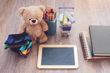 Back to school background with slate blackboard, pencils on bin toy, chalks in shopping cart and kids shocks on wooden table, Education concept