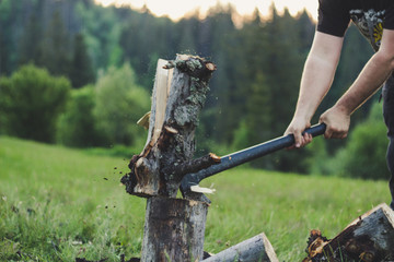 The guy is cutting an old tree in the mountains with an ax. Ukrainian Carpathian Mountains. Bonfire. Tourism. Ax