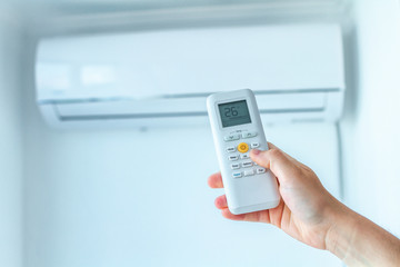 Air conditioner temperature adjustment with remote controller in room at home.