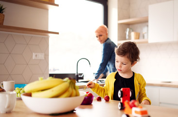 A young mother with small daughter eating fruit in a kitchen.