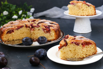 Plums pie is located on a plate on a dark background, piece of cake in the foreground, Fresh plums are on the table