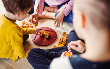 A midsection of mother with two children playing board games on the floor.