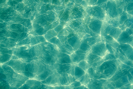 The sun pattern is a play of light and shadow in the form of highlights, spots and streaks on the calm clear surface of the emerald transparent sea water