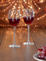 Two glasses with red wine on a wooden table, Glittering bokeh background. Red grapes out of focus in foreground.
