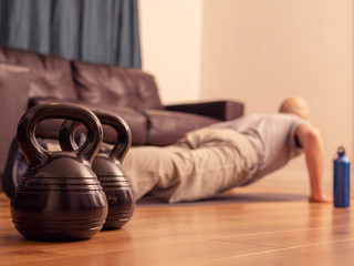 Kettle bell in focus, bold man doing push ups on a floor. Concept workout at home, fitness.