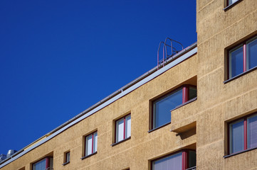 Yellow apartment building exterior red frame windows with handrail on the roof and blue sky