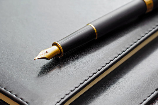 macro of black luxury gold plated fountain pen on leather notebook cover - Powered by Adobe