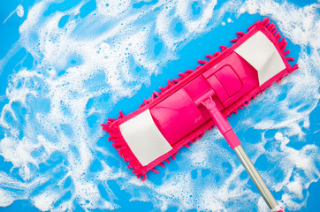 Flat lay cleaning with mop concept. Pink microfiber mop with soapy water on a light blue background