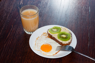 Healthy, tasty breakfast, juice, wholemeal bread sandwich with kiwi and a fried egg on a white plate, on a wooden table