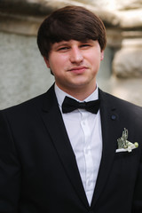Portrait of handsome groom in black suit with tie bow