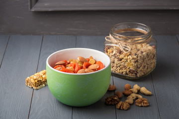 Granola cereal flakes with dried fruit, nuts in green bowl on gray wooden table.