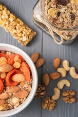Granola cereal flakes with dried fruit, nuts in green bowl on gray wooden table. Top view.