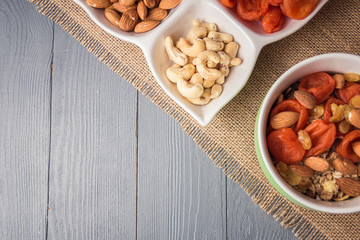Granola cereal flakes with dried fruit, nuts in green bowl on gray wooden table. Top view with copyspace.