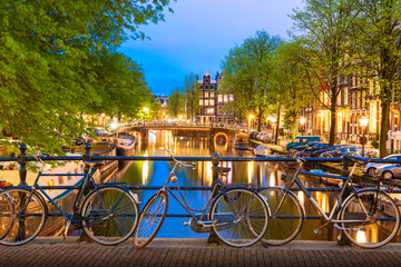 Old bicycles on the bridge in Amsterdam, Netherlands against a canal during summer twilight sunset. Amsterdam postcard iconic view. Tourism concept. - obrazy, fototapety, plakaty