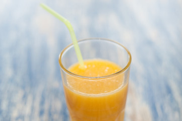 Orange juice in a glass with a straw on a blue wooden background of aqua color, top view and side view close-up