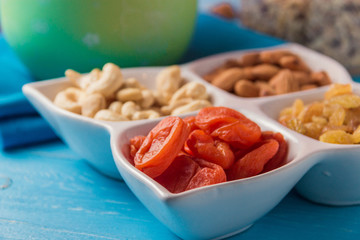 Granola cereal flakes with dried fruit, nuts in plate on blue wooden table.