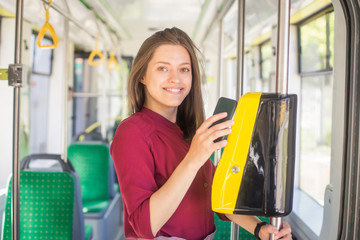 Female Woman paying conctactless with smartphone for the public transport in the tram. Yellow...