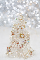 Fototapeta na wymiar White Christmas tree with pearls and beads on the snow next to beautiful blurred bokeh background and glowing garland. Copy space.