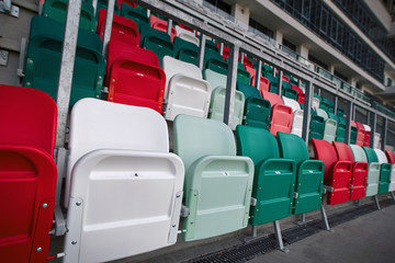 Fototapeta premium Rows of empty multicolored plastic stadium seats. Empty seats on tribune arena. Football stadium bleachers. Soccer, football stadium tribune without fans. Empty tribunes, game over. Sport Concept