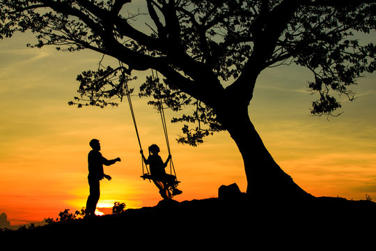 The silhouette of tourists playing swings with big trees, couples and swings during the sunset, concept travel with nature.