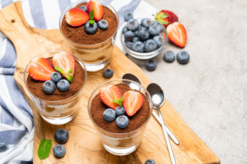 Fototapeta na wymiar Classic tiramisu dessert with blueberries and strawberries in a glass on concrete background