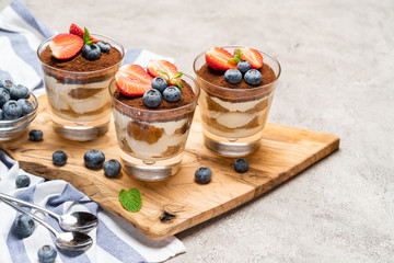 Classic tiramisu dessert with blueberries and strawberries in a glass on concrete background