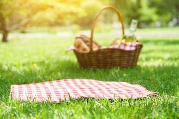 Wicker picnic basket with food and red tablecloth on the grass.