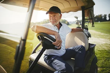 Poster Senior man sitting in his golf cart on a fairway © Flamingo Images